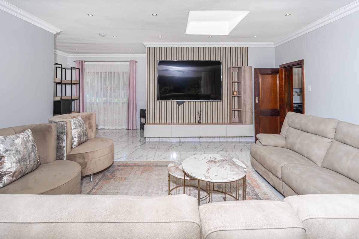 Spacious living room featuring a modern slatted feature wall with built-in cabinetry, polished marble-look floor tiles, and a skylight providing natural illumination.