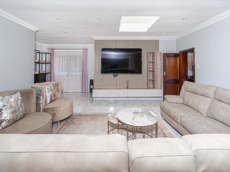 Spacious living room featuring a modern slatted feature wall with built-in cabinetry, polished marble-look floor tiles, and a skylight providing natural illumination.