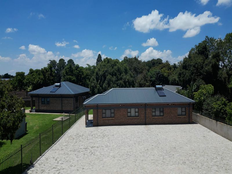 Aerial view of a property featuring two brick buildings with metal roofs, solar geysers, and a large paved driveway area.