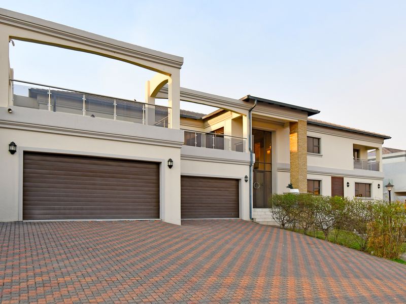 Modern double-story residence featuring a paved driveway, double garage, and an upper-level balcony with glass balustrades and stone architectural accents.