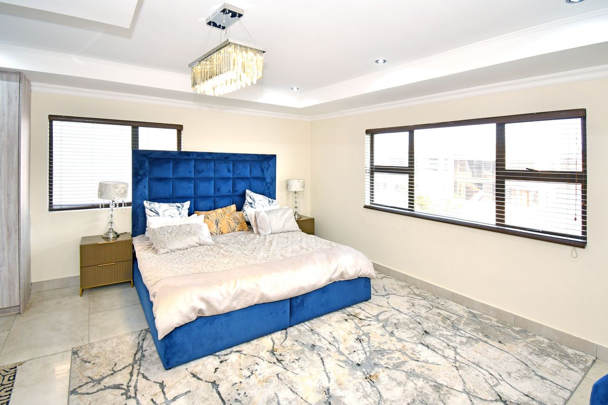 Spacious bedroom featuring a tray ceiling with recessed lighting, large windows with venetian blinds, and neutral tiled flooring.