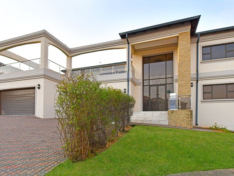 Modern double-storey residence featuring a paved driveway, double garage, stone-clad entrance pillar, and an expansive upper-level balcony with glass balustrades.