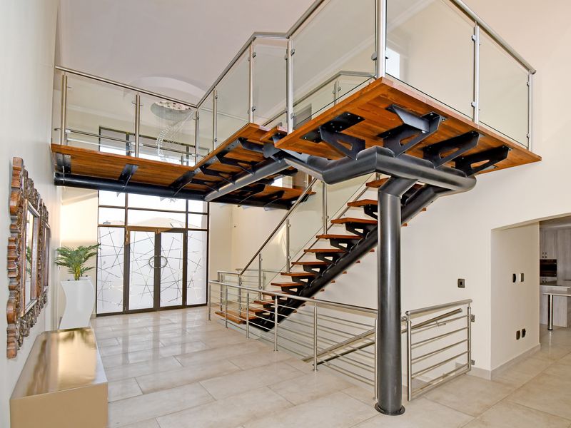 A grand double-volume entrance hall featuring a striking floating staircase with glass balustrades and modern tiled flooring.