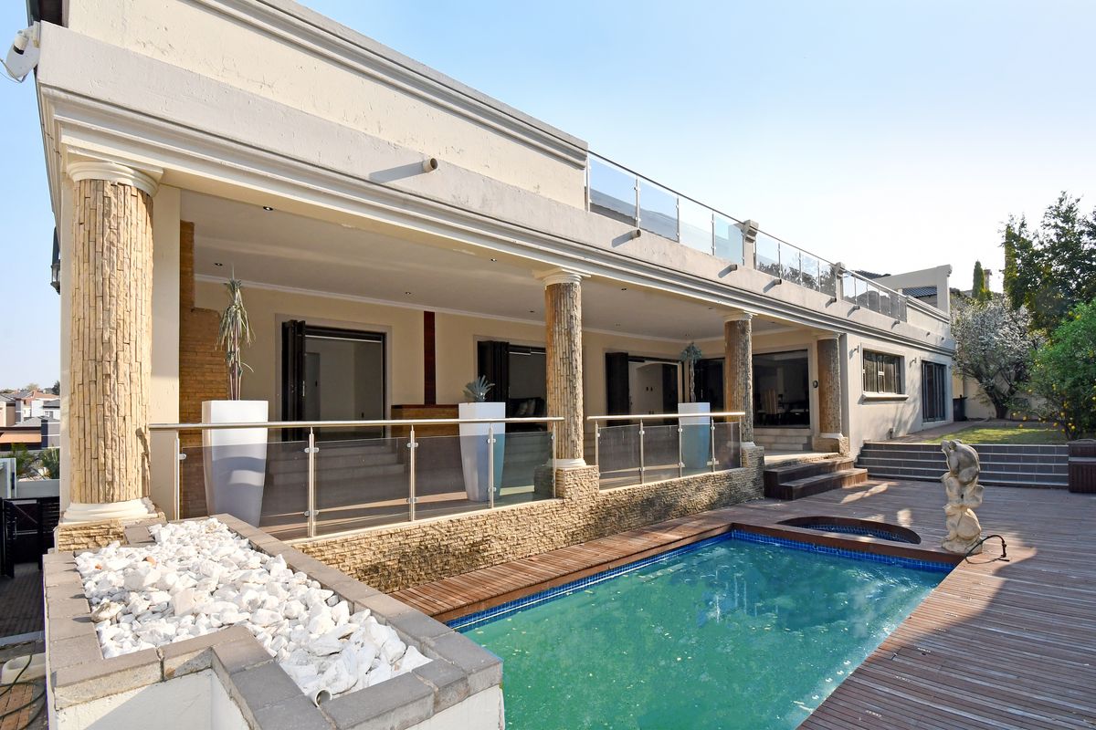 Spacious rear exterior featuring a swimming pool, wooden decking, stone-clad columns, and a covered patio with glass balustrades and bi-fold doors.