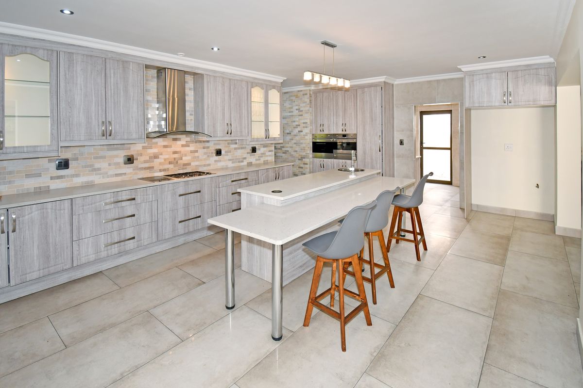 Modern kitchen featuring light wood-grain cabinetry, stone countertops, a central island with breakfast bar, and high-quality built-in appliances.