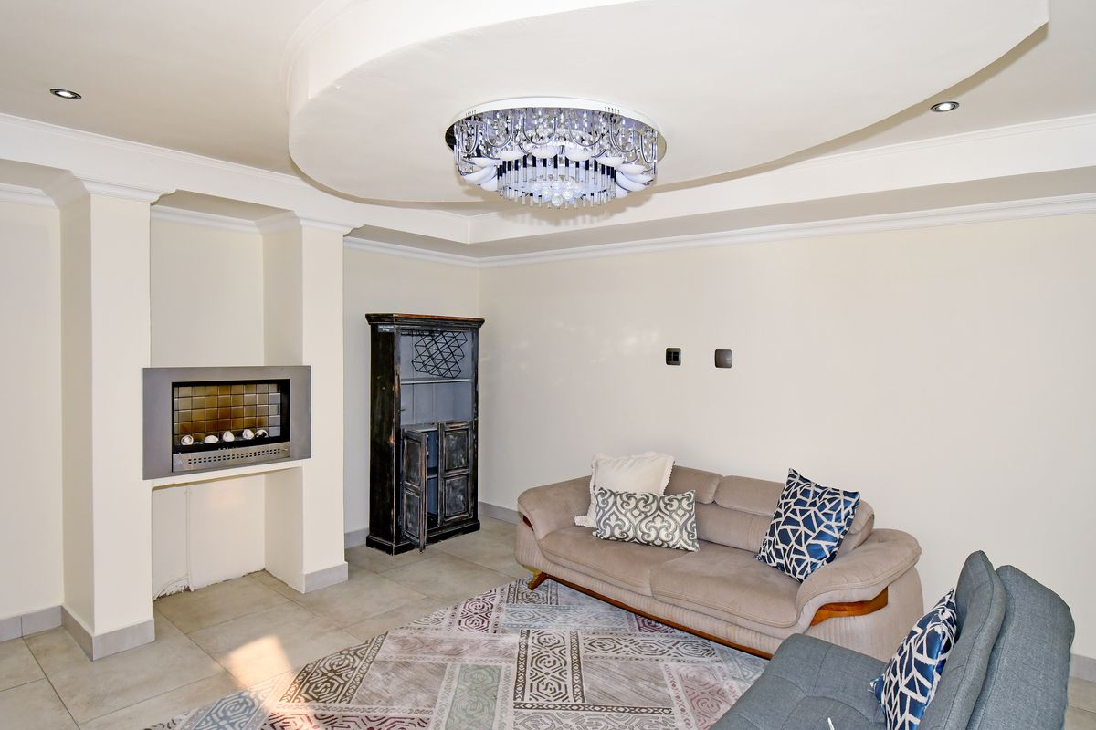 A living room featuring a recessed fireplace, a decorative coffered ceiling with a crystal chandelier, and neutral tiled flooring.
