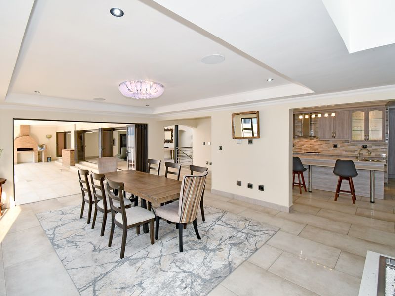 Spacious open-plan living and dining area featuring tiled floors, recessed ceiling lighting, and a modern kitchen with stone countertops, flowing onto a covered patio.