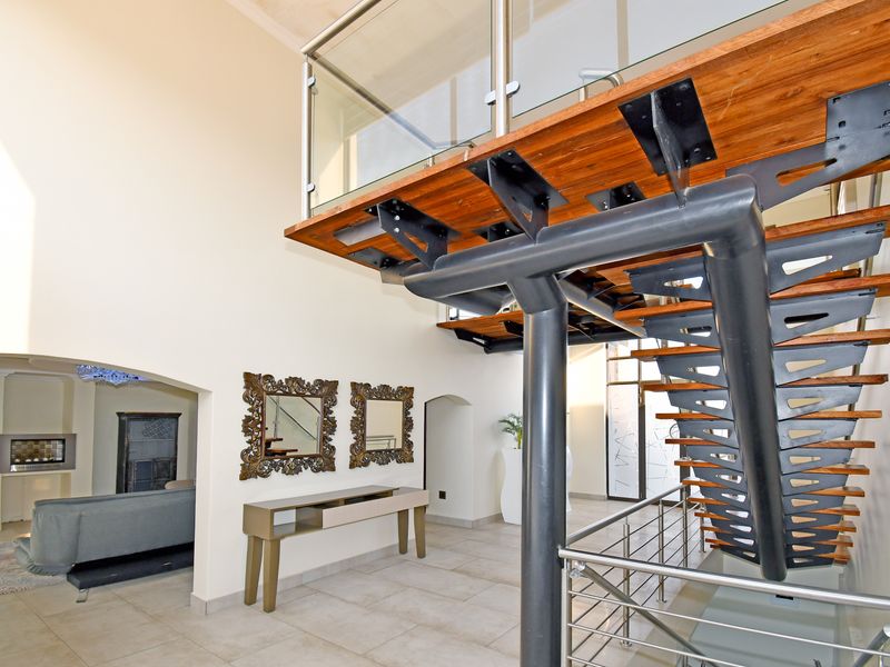 Spacious entrance hall featuring a modern floating staircase with timber treads, glass balustrades, and a recessed fireplace in the adjacent living area.