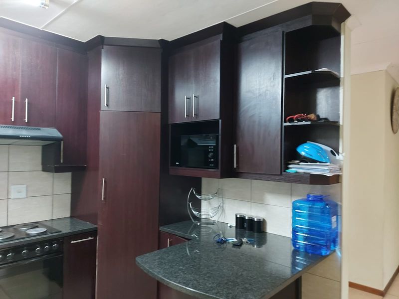 A functional kitchen featuring dark wood cabinetry, granite countertops, and integrated appliances including an oven, hob, and microwave.