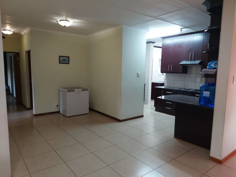 Open plan kitchen and living area featuring dark wood cabinetry, granite countertops, built-in oven, extractor fan, and neutral ceramic floor tiles.