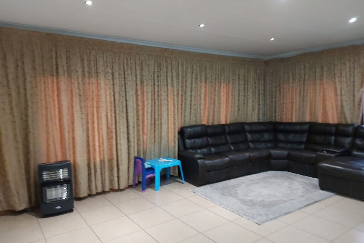 Spacious living room featuring neutral ceramic floor tiles, recessed downlighting, and full-length window treatments.