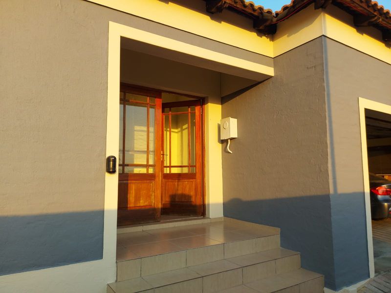 Front entrance featuring tiled steps and a timber-framed glass door, set against a grey rendered facade with warm sunset lighting.