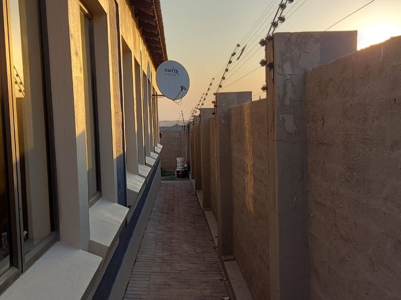 A narrow side passage featuring brick paving, a high boundary wall with electric fencing, and exterior wall access.