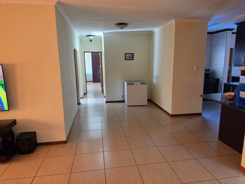 Open plan living area featuring neutral ceramic floor tiles, coved cornicing, and direct access to adjacent rooms and kitchen space.