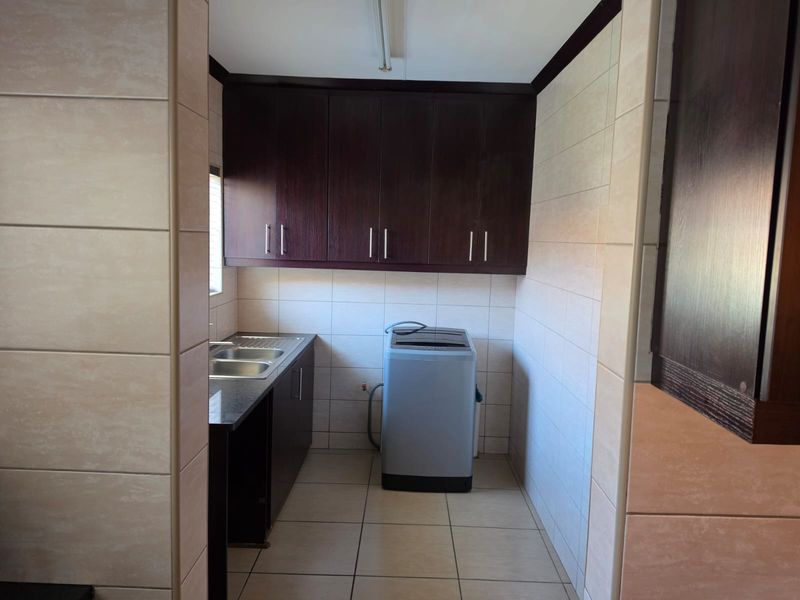 A functional laundry room featuring built-in dark wood cabinetry, a stainless steel sink, and tiled finishes throughout.