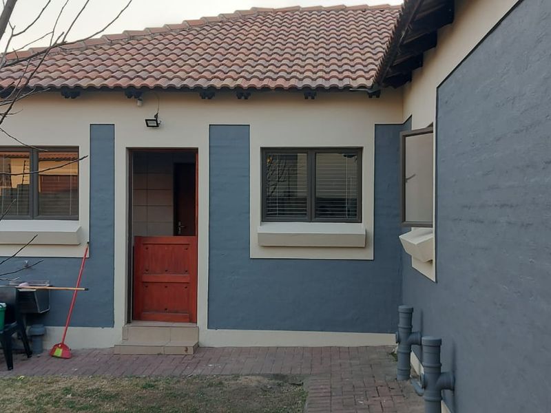 Rear elevation of the house featuring painted masonry walls, terracotta roof tiles, a timber stable door, and a paved patio area.