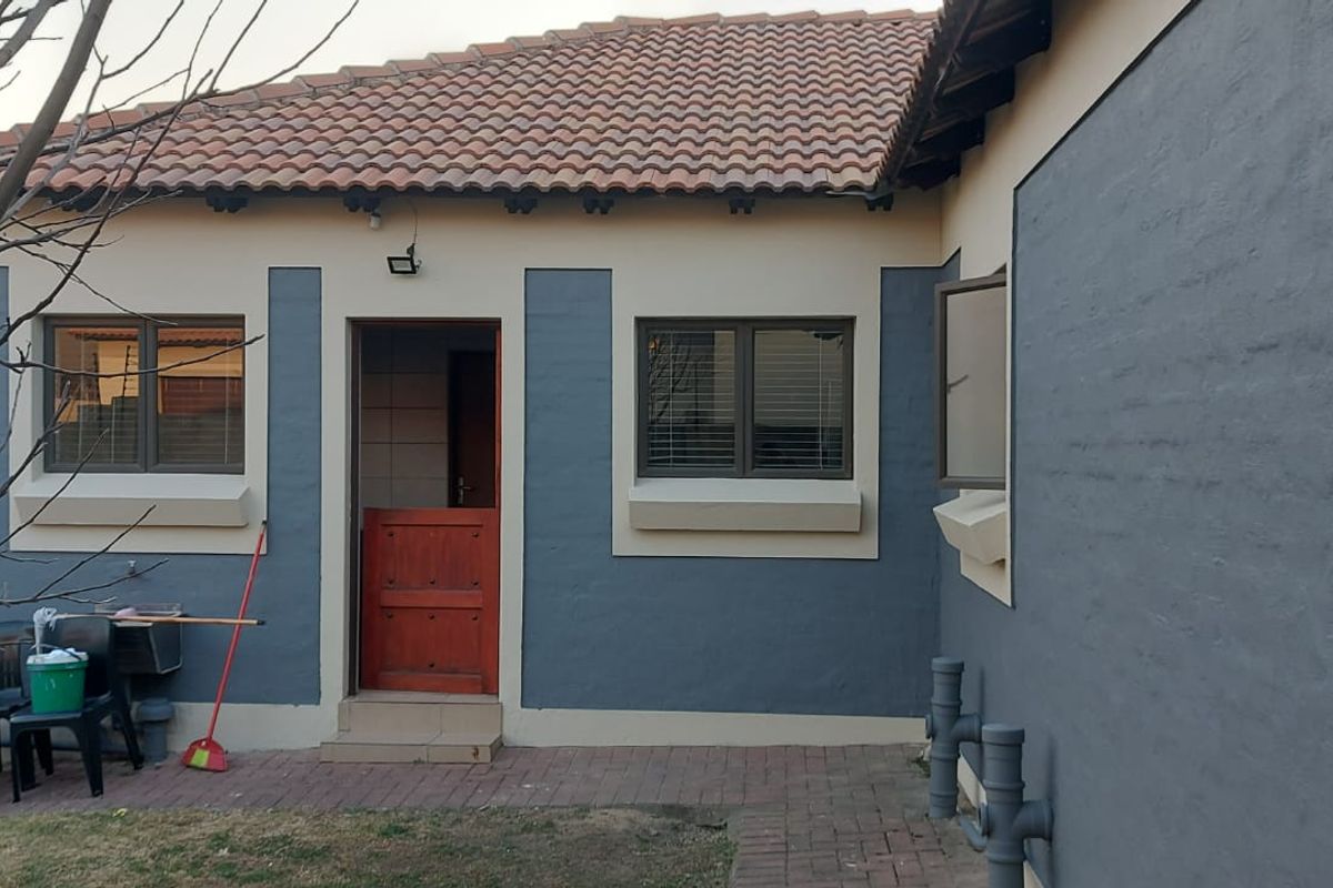 Rear elevation of the house featuring painted masonry walls, terracotta roof tiles, a timber stable door, and a paved patio area.