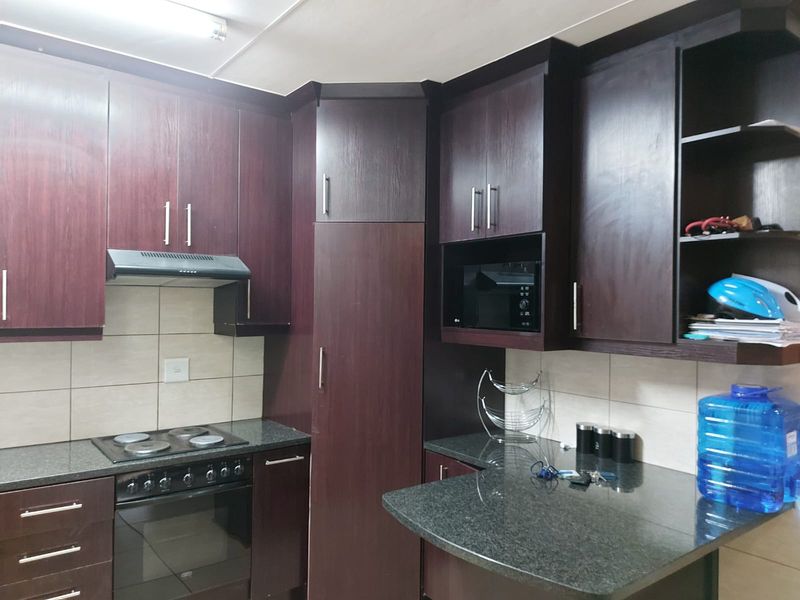 A functional kitchen featuring dark wood cabinetry, granite countertops, a built-in oven, electric hob, and a tiled backsplash.