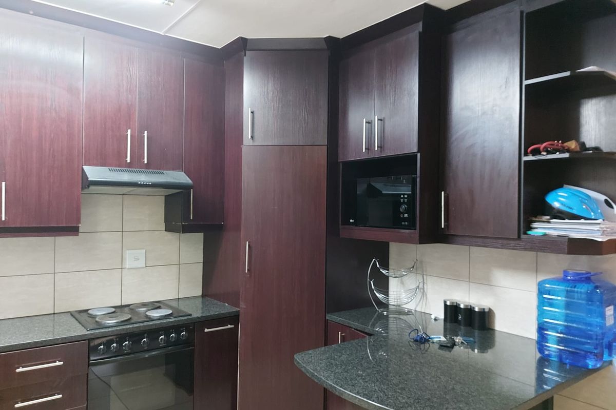 A functional kitchen featuring dark wood cabinetry, granite countertops, a built-in oven, electric hob, and a tiled backsplash.