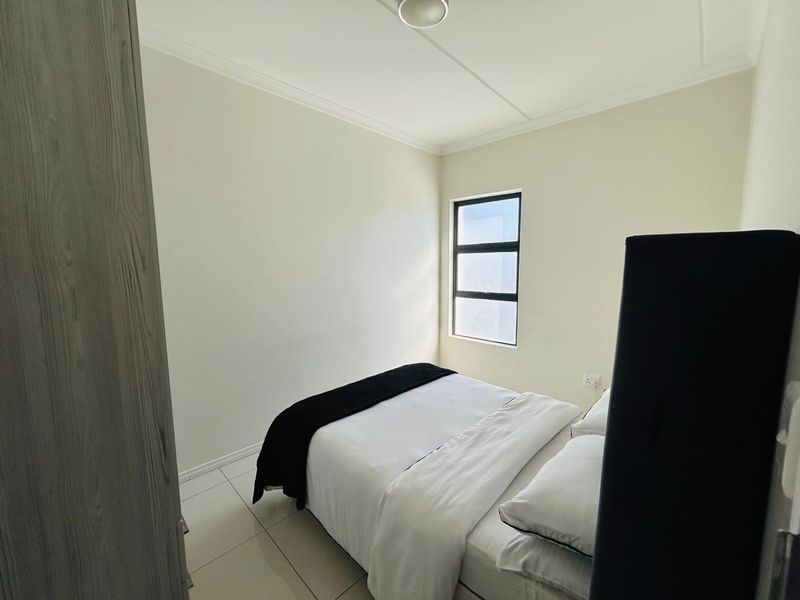 A clean, neutral bedroom featuring tiled flooring, a built-in cupboard, and a window allowing natural light.
