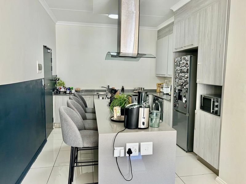 Modern kitchen featuring a central island with breakfast bar seating, sleek cabinetry, stone countertops, and integrated appliances including a built-in microwave and extractor fan.