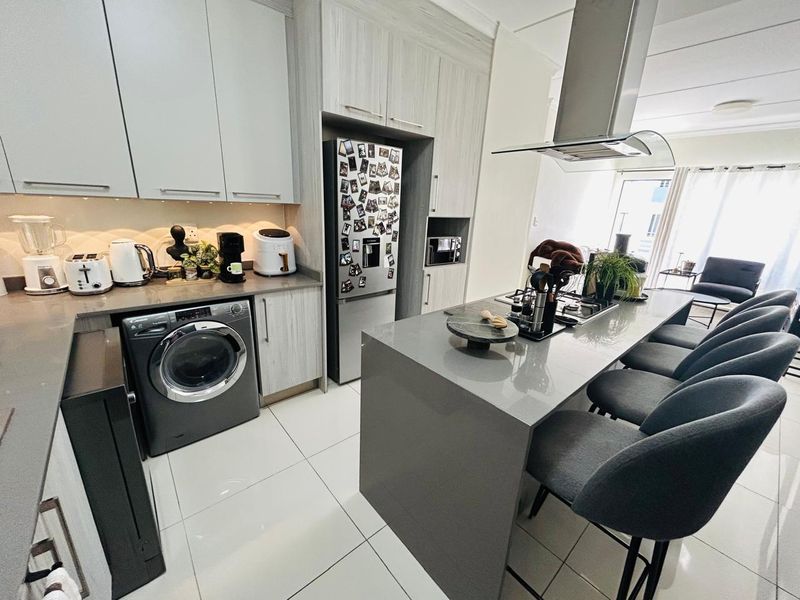 Modern kitchen featuring sleek cabinetry, stone countertops, a central island with breakfast bar seating, and integrated appliances including a washing machine.