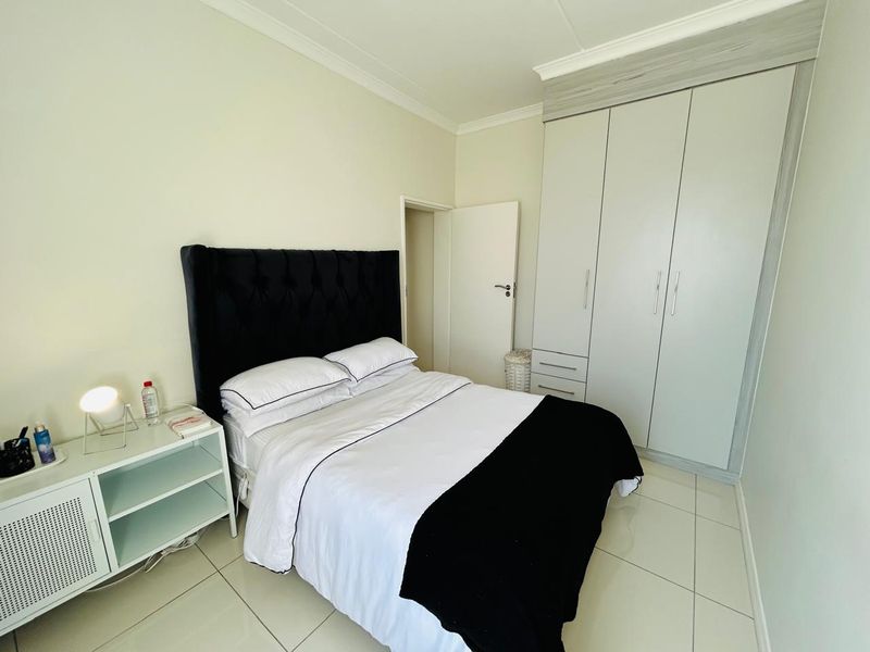 A well-maintained bedroom featuring neutral tiled flooring, a built-in wardrobe with overhead storage, and classic cornice detailing.