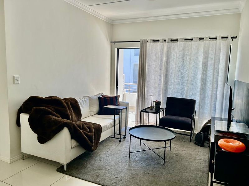 A bright living room featuring tiled flooring and a sliding glass door that provides access to an outdoor balcony area.