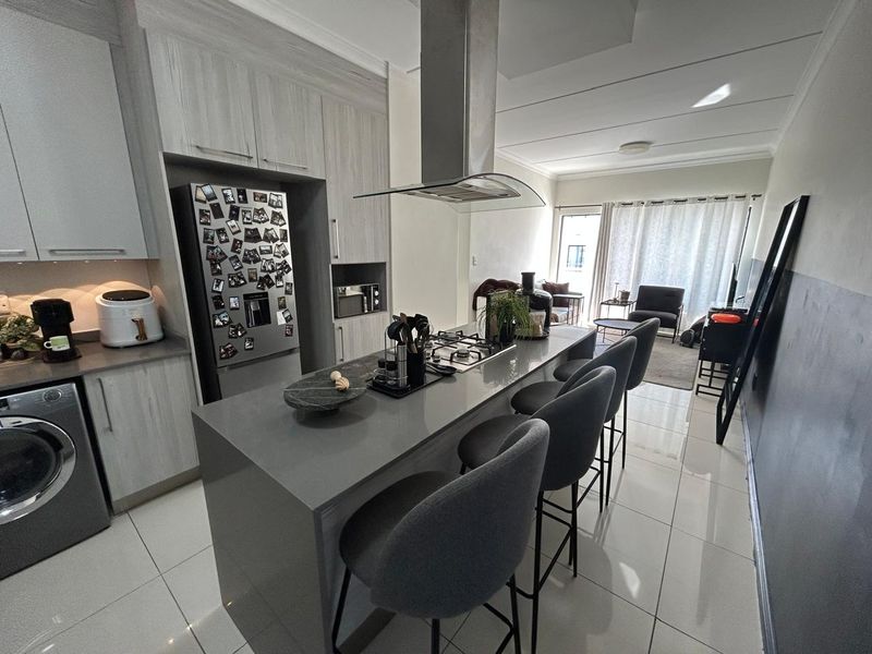 Modern open-plan kitchen and living area featuring a central island with gas hob, sleek cabinetry, and polished tile flooring throughout.