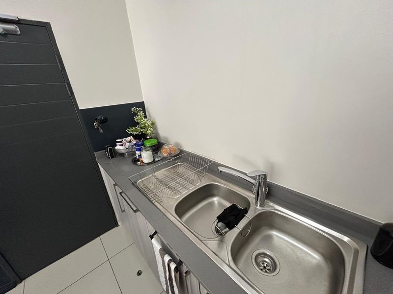 A compact kitchen area featuring a double bowl stainless steel sink, chrome mixer tap, stone countertop, and modern built-in cabinetry.