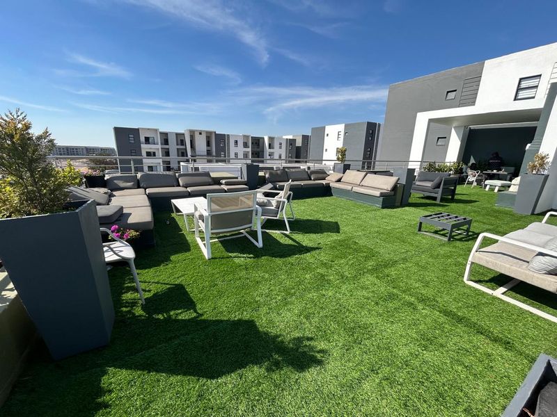 Spacious rooftop terrace featuring artificial turf flooring and modern metal railings, offering an open-air outdoor living space.