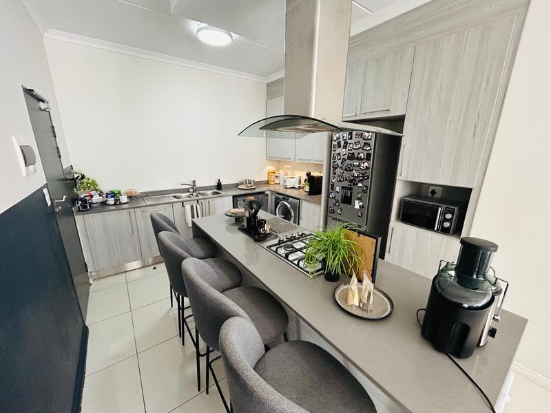 Modern kitchen featuring light wood-grain cabinetry, stone countertops, a central breakfast bar with integrated gas hob, and sleek tiled flooring.