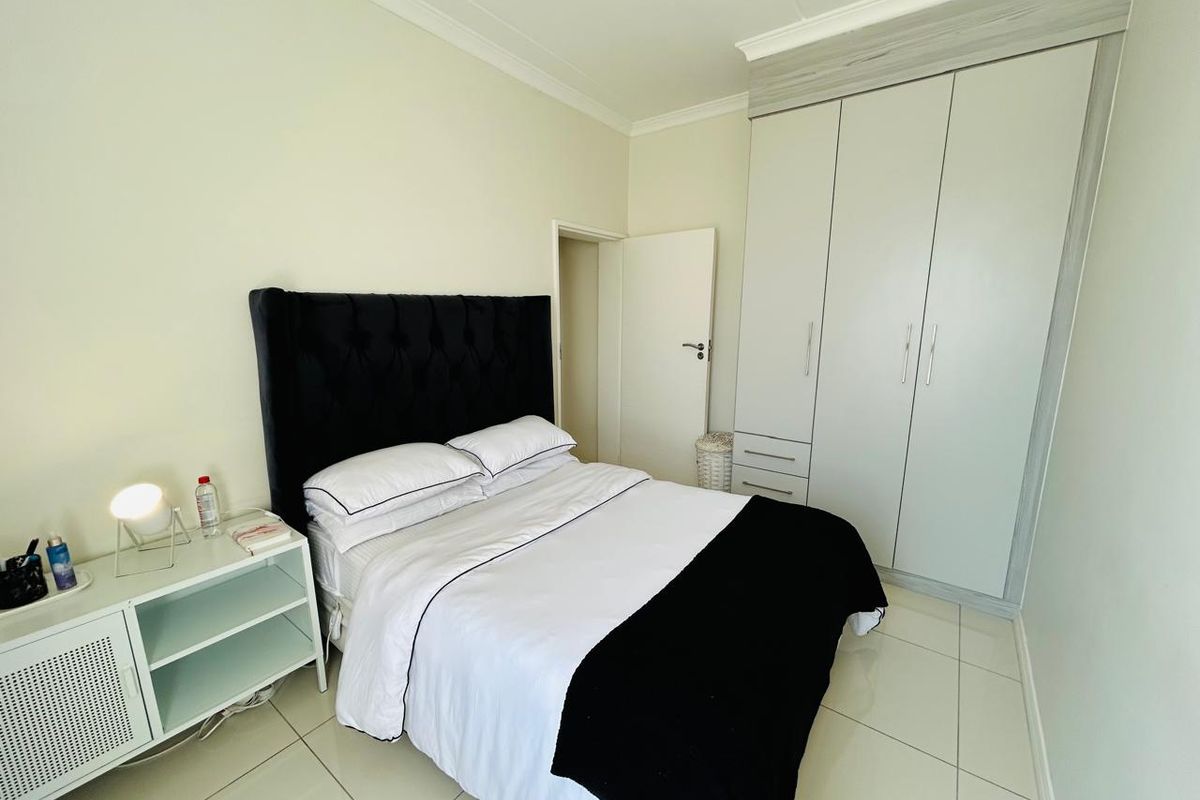 A well-maintained bedroom featuring neutral tiled flooring, a built-in wardrobe with overhead storage, and classic cornice detailing.