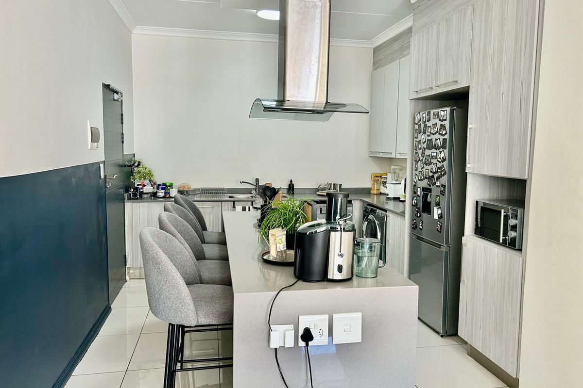 Modern kitchen featuring a central island with breakfast bar seating, sleek cabinetry, stone countertops, and integrated appliances including a built-in microwave and extractor fan.