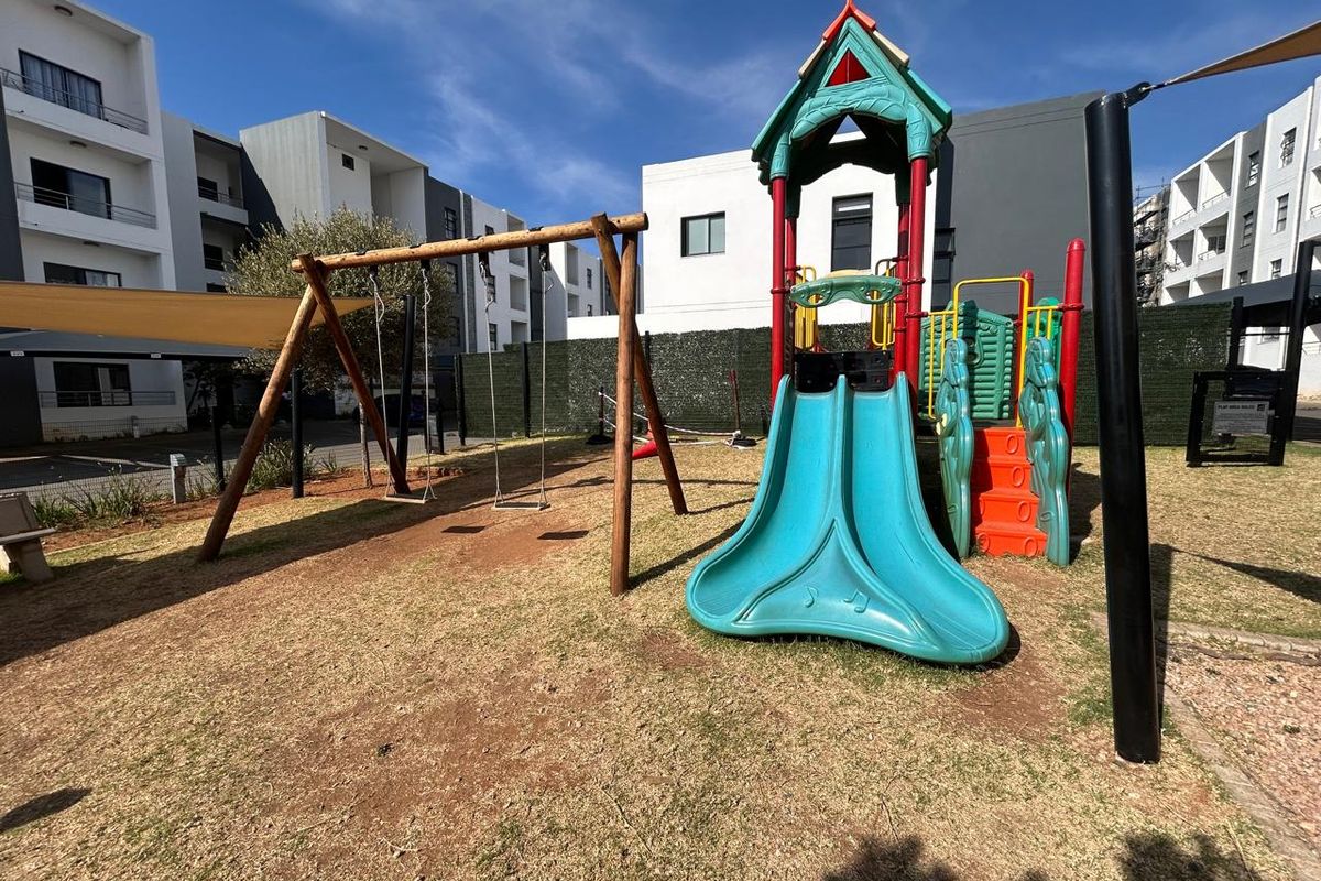Communal outdoor playground area featuring a slide, swing set, and shade sail, situated within an apartment complex.