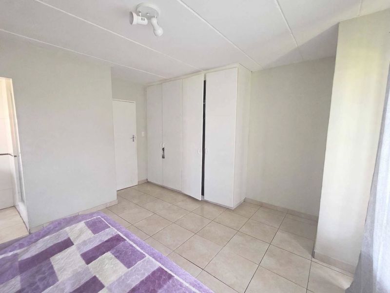 A bedroom featuring neutral tiled flooring, white walls, and built-in cupboards providing ample storage space.