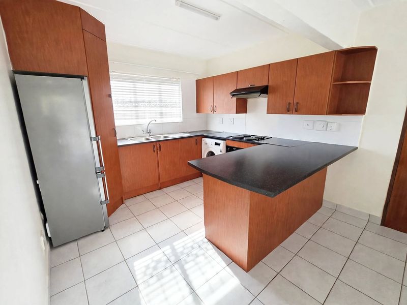 A functional kitchen featuring wood-look laminate cabinetry, dark countertops, a built-in hob with extractor fan, and tiled flooring.