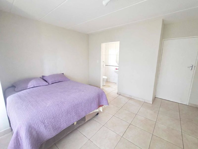 A bedroom featuring tiled flooring and direct access to an en-suite bathroom, offering a neutral and functional living space.