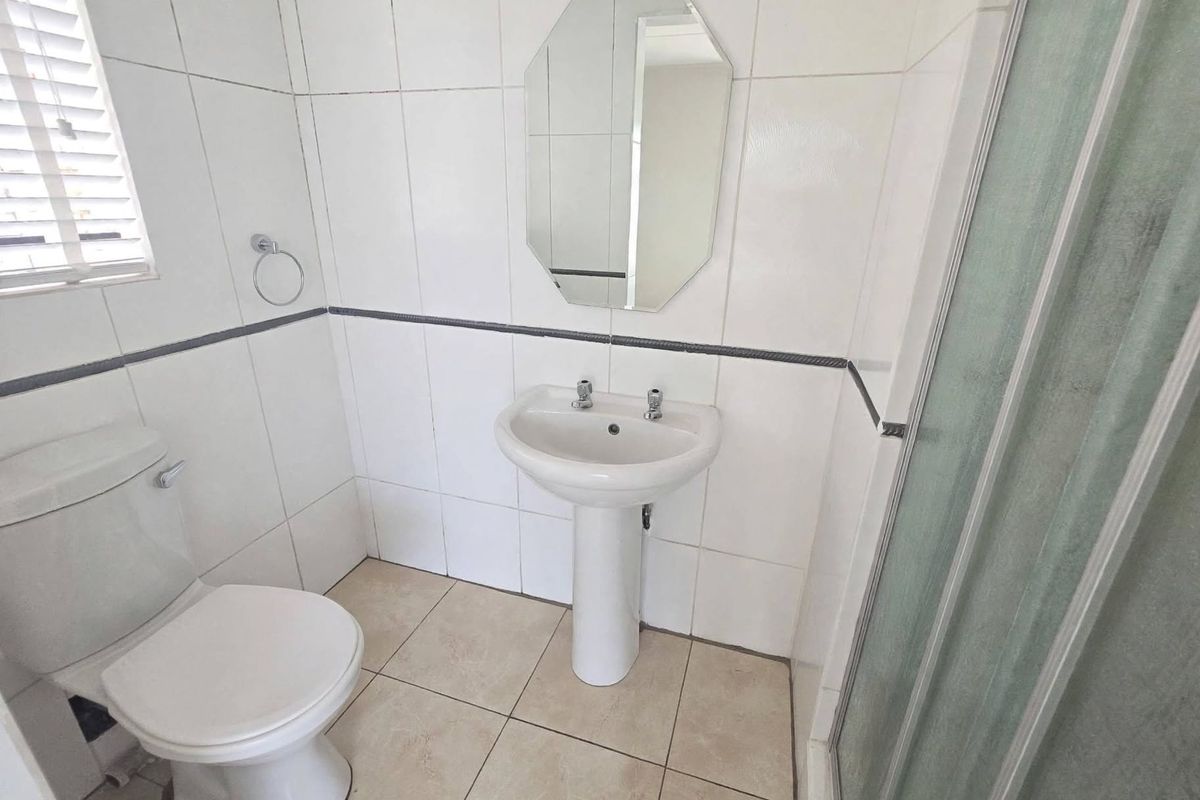 A functional bathroom featuring a pedestal basin, toilet, and shower enclosure with neutral wall and floor tiling.