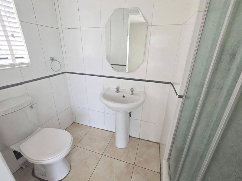 A functional bathroom featuring a pedestal basin, toilet, and shower enclosure with neutral wall and floor tiling.