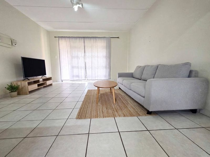 A simple living room featuring neutral tiled flooring and a sliding glass door that provides access to the exterior.