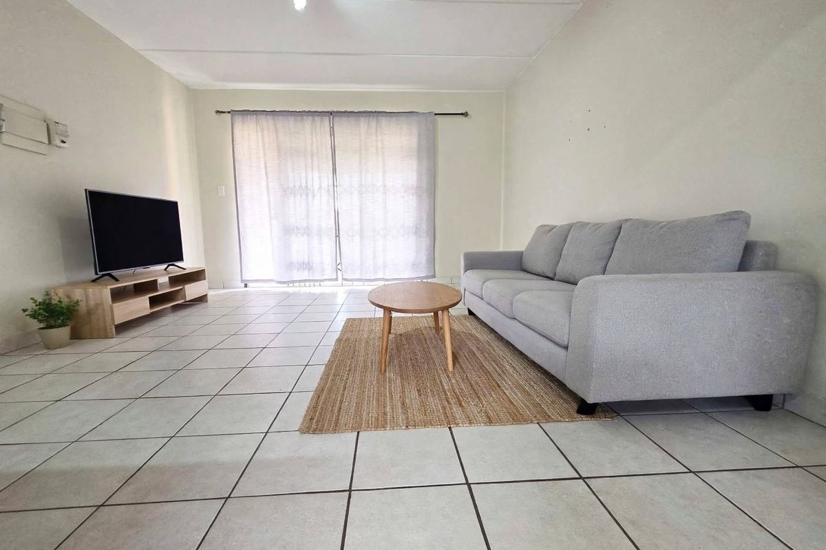 A simple living room featuring neutral tiled flooring and a sliding glass door that provides access to the exterior.