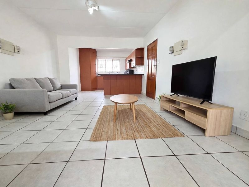 Open plan living area featuring ceramic floor tiles and a functional kitchen with built-in cabinetry and a breakfast bar.