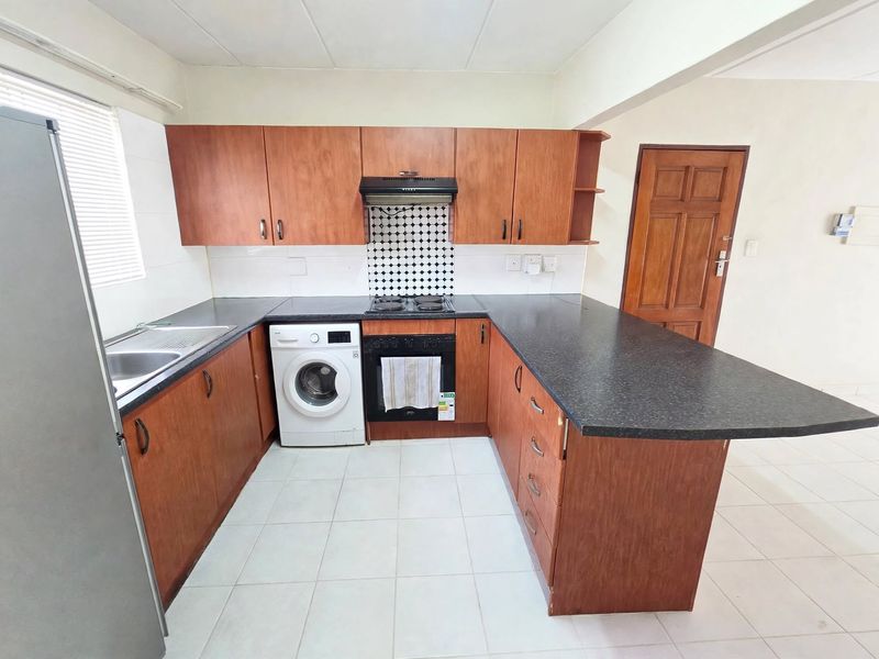 Functional kitchen featuring wood-look cabinetry, dark laminate countertops, built-in oven with hob, and tiled flooring with an integrated laundry appliance space.