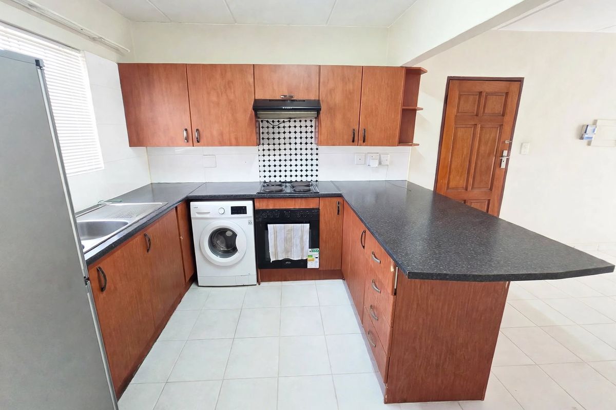 Functional kitchen featuring wood-look cabinetry, dark laminate countertops, built-in oven with hob, and tiled flooring with an integrated laundry appliance space.