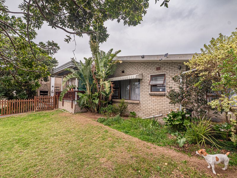 Rear view of the property featuring a brick facade, timber fencing, and a landscaped garden area with established trees and shrubs.