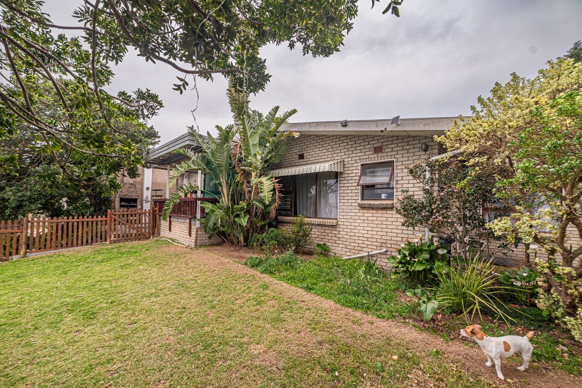 Rear view of the property featuring a brick facade, timber fencing, and a landscaped garden area with established trees and shrubs.