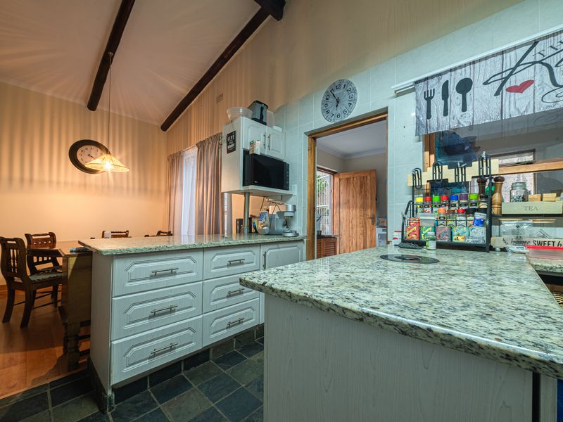 Kitchen featuring granite countertops, built-in cabinetry, and exposed timber ceiling beams, with an open-plan layout connecting to the dining area.