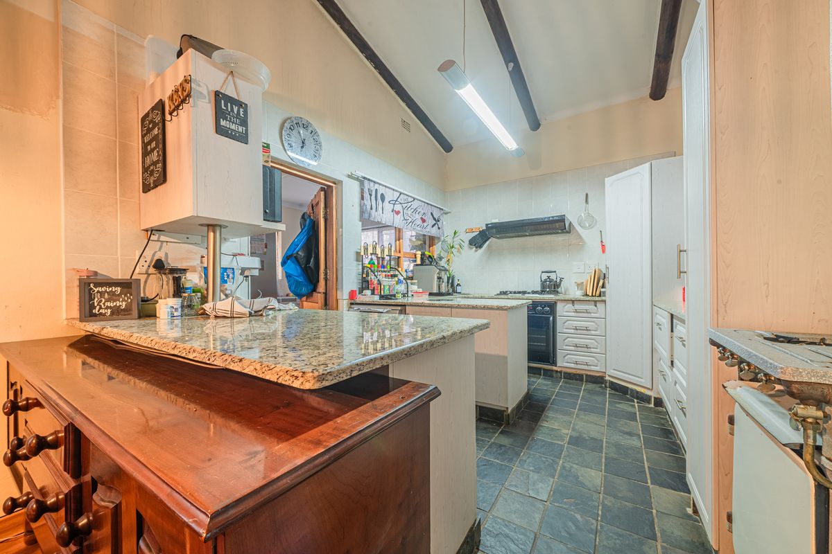 A functional kitchen featuring granite countertops, slate tile flooring, exposed ceiling beams, and built-in cabinetry with an integrated oven and extractor fan.