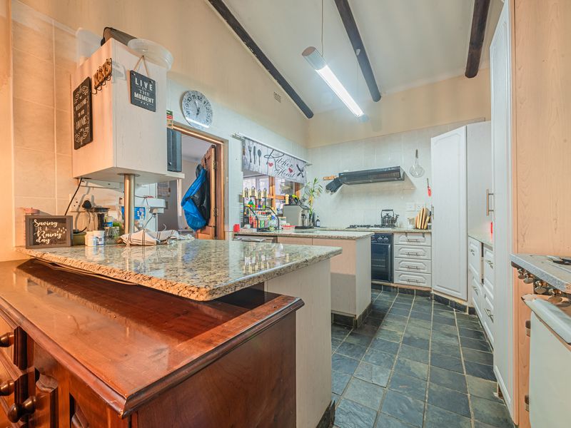 A functional kitchen featuring granite countertops, slate tile flooring, exposed ceiling beams, and built-in cabinetry with an integrated oven and extractor fan.